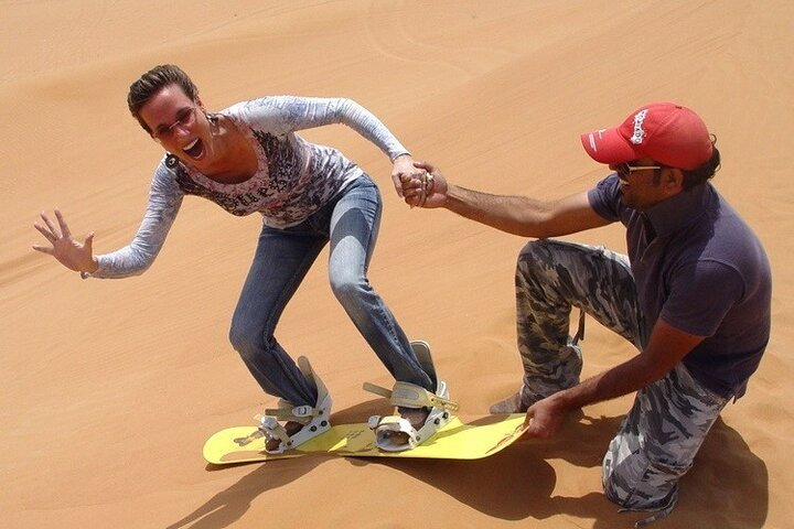 Experience the thrill of sandboarding on the golden dunes as a local guide lends a hand showcasing the excitement and charm of the Abu Dhabi desert landscape.